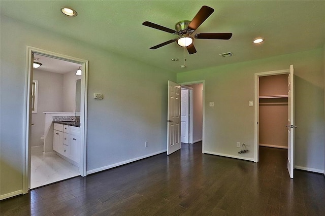 unfurnished bedroom featuring dark wood-type flooring, ensuite bathroom, ceiling fan, a closet, and a spacious closet