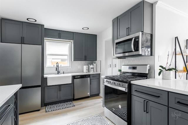 kitchen featuring sink, stainless steel appliances, tasteful backsplash, gray cabinets, and light wood-type flooring