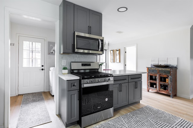 kitchen featuring washer and clothes dryer, gray cabinetry, decorative backsplash, light wood-type flooring, and appliances with stainless steel finishes