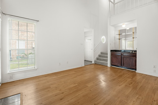 unfurnished living room featuring light hardwood / wood-style flooring and a towering ceiling