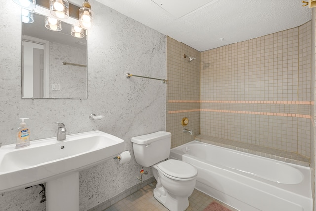 full bathroom featuring sink, tiled shower / bath combo, toilet, and a textured ceiling