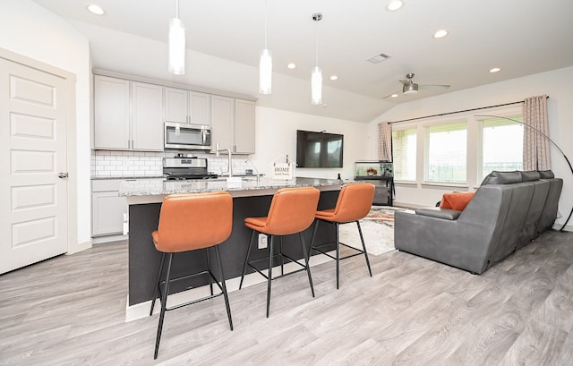 kitchen featuring stainless steel appliances, hanging light fixtures, an island with sink, and light stone counters