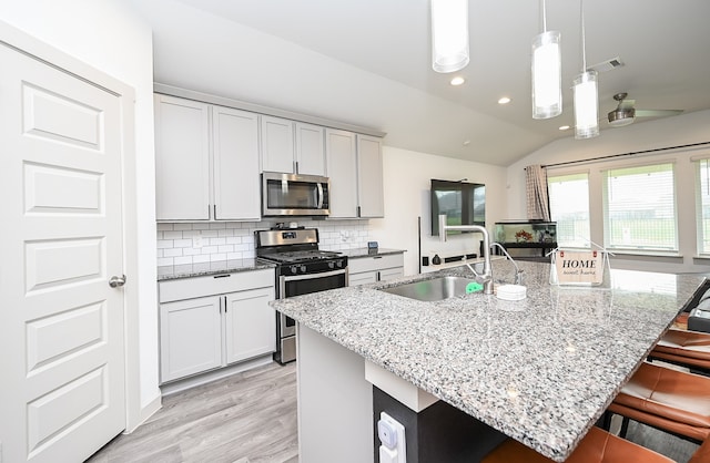 kitchen featuring lofted ceiling, a center island with sink, hanging light fixtures, a breakfast bar, and appliances with stainless steel finishes