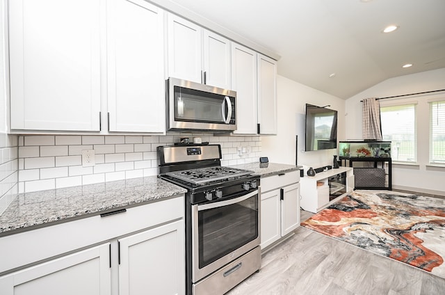 kitchen with appliances with stainless steel finishes, backsplash, white cabinets, light wood-type flooring, and vaulted ceiling