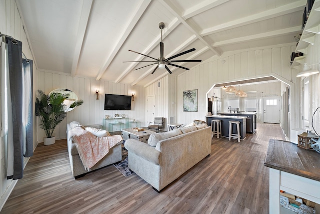 living room featuring dark wood-type flooring, wooden walls, sink, ceiling fan, and lofted ceiling with beams