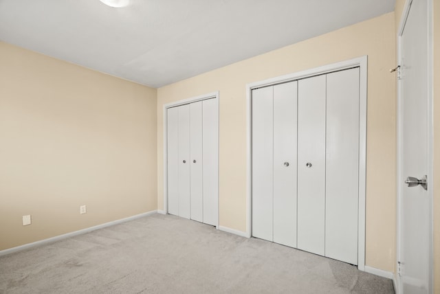 unfurnished bedroom featuring multiple closets and light carpet