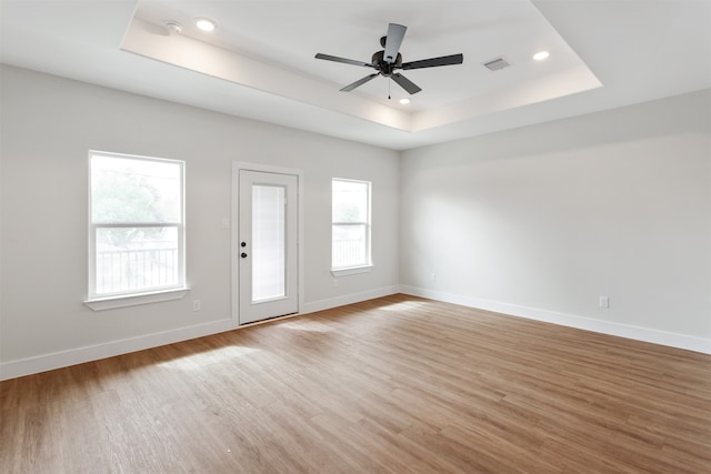 unfurnished room with light hardwood / wood-style floors, ceiling fan, and a raised ceiling