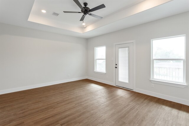 interior space with ceiling fan, wood-type flooring, and a tray ceiling