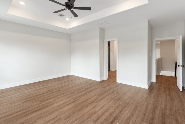 spare room with ceiling fan, wood-type flooring, and a tray ceiling