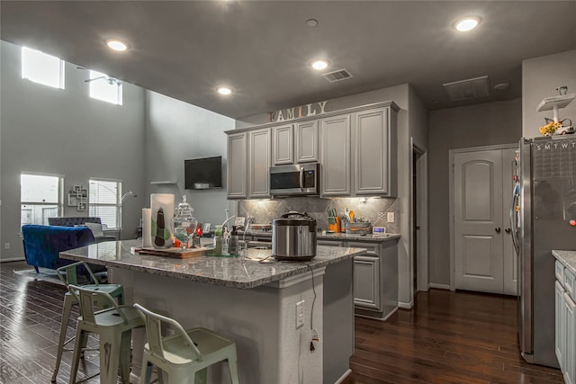 kitchen featuring a center island with sink, light stone counters, appliances with stainless steel finishes, dark hardwood / wood-style floors, and a breakfast bar area