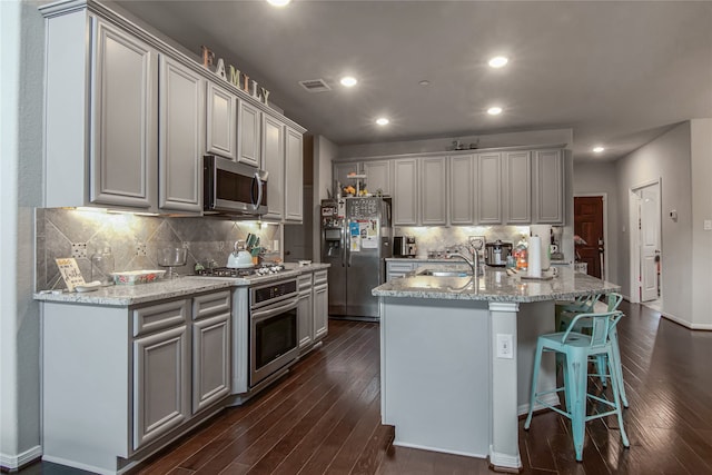 kitchen with an island with sink, dark hardwood / wood-style flooring, appliances with stainless steel finishes, and tasteful backsplash