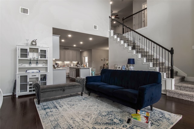 living room with dark hardwood / wood-style flooring, ceiling fan, and a towering ceiling