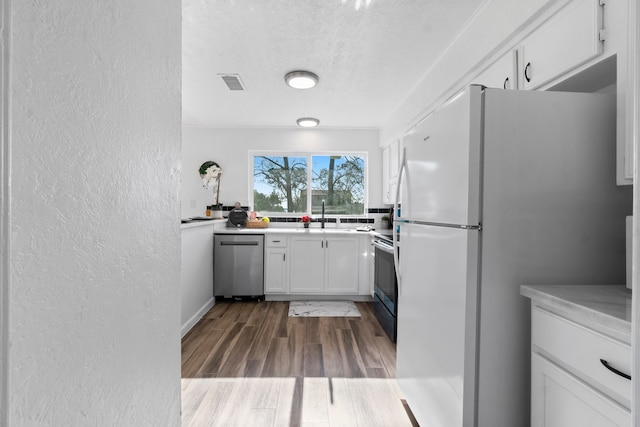 kitchen featuring white cabinets, sink, a textured ceiling, appliances with stainless steel finishes, and wood-type flooring