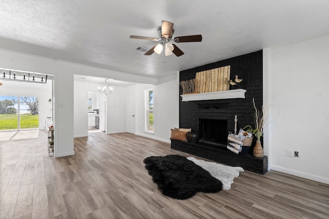 living room with a fireplace, plenty of natural light, wood-type flooring, and ceiling fan with notable chandelier