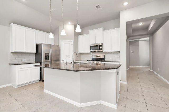 kitchen featuring stainless steel appliances, light tile patterned flooring, a center island with sink, white cabinets, and decorative backsplash