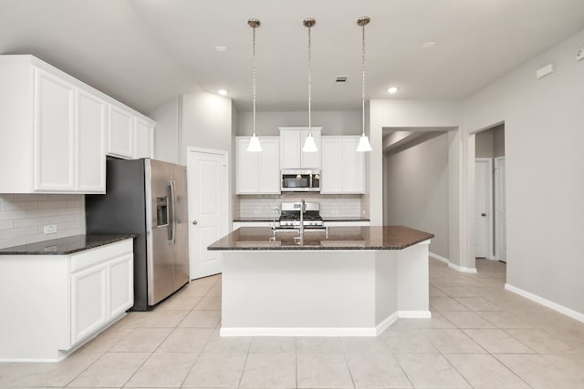 kitchen featuring pendant lighting, stainless steel appliances, dark stone counters, and an island with sink