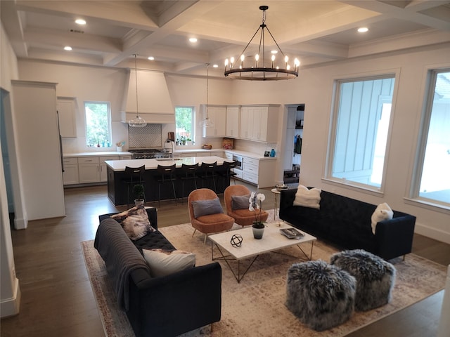 living room with dark hardwood / wood-style flooring, coffered ceiling, an inviting chandelier, and beamed ceiling