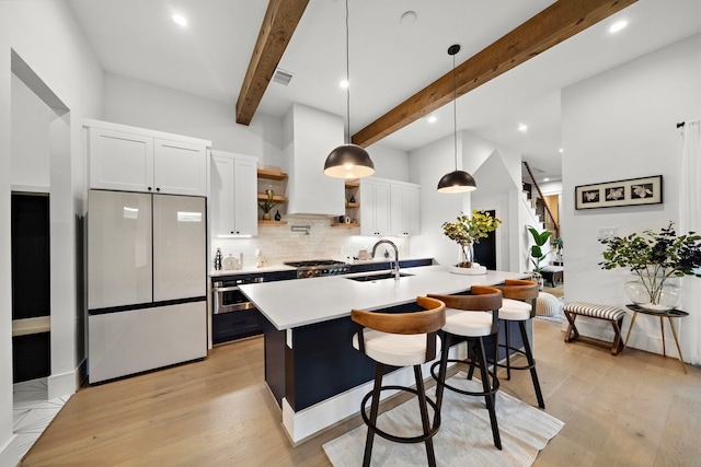 kitchen featuring sink, hanging light fixtures, stainless steel appliances, a kitchen island with sink, and white cabinets