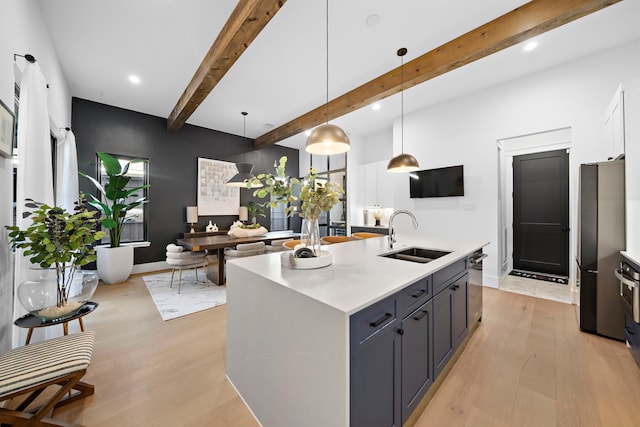 kitchen featuring white cabinetry, sink, hanging light fixtures, a kitchen island with sink, and light wood-type flooring