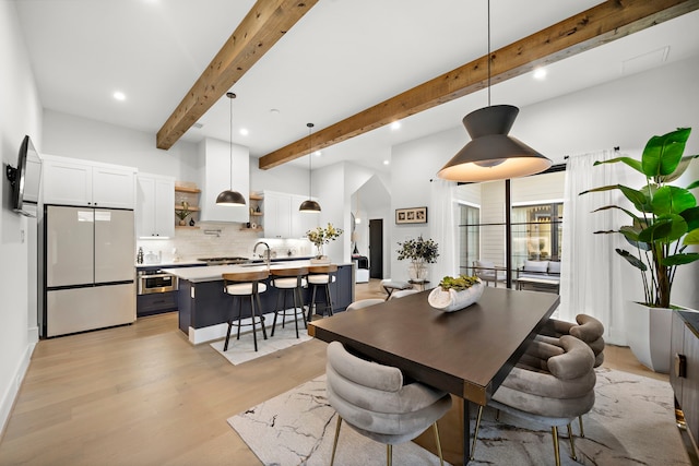 dining area featuring beam ceiling, light hardwood / wood-style floors, and sink