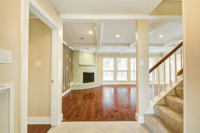 unfurnished living room featuring a brick fireplace, beam ceiling, light hardwood / wood-style flooring, and a textured ceiling