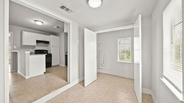 kitchen with white cabinetry, light tile patterned floors, black gas range oven, and light stone countertops