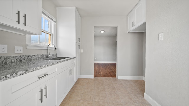 kitchen with white cabinetry, sink, light tile patterned floors, and light stone countertops