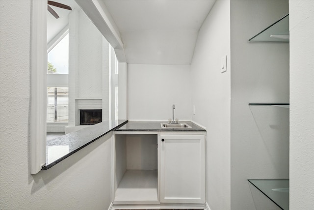 kitchen with white cabinetry, a large fireplace, sink, and ceiling fan