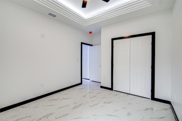 unfurnished bedroom featuring a closet, a tray ceiling, and ceiling fan