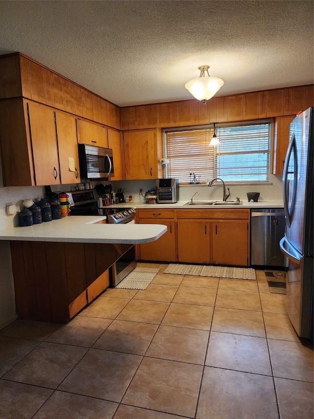 kitchen with light tile patterned flooring, stainless steel appliances, a textured ceiling, decorative light fixtures, and sink