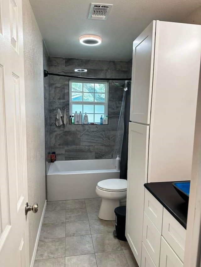 full bathroom featuring tile patterned floors, toilet, tiled shower / bath, a textured ceiling, and vanity