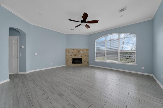 unfurnished living room with a stone fireplace, ceiling fan, and crown molding