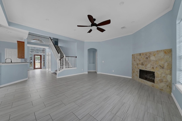 unfurnished living room featuring ceiling fan, a stone fireplace, and crown molding