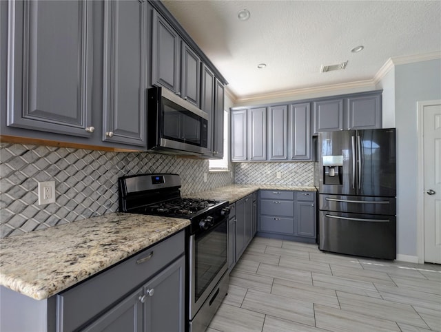 kitchen featuring gray cabinetry, light stone countertops, backsplash, crown molding, and appliances with stainless steel finishes