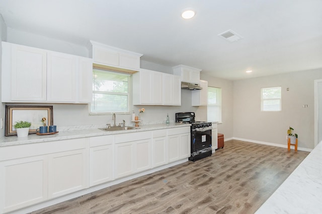 kitchen with light wood-type flooring, light stone counters, sink, black range, and white cabinets