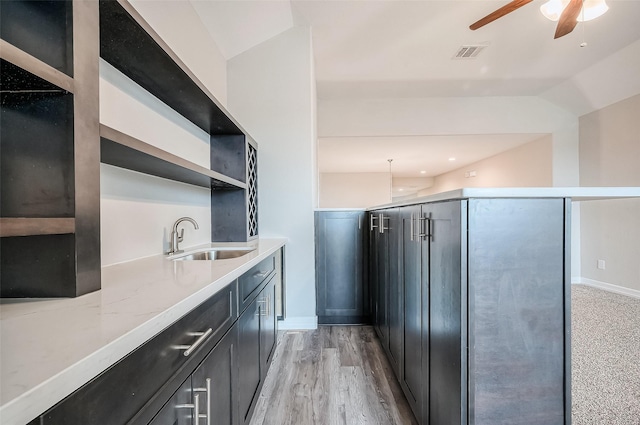 kitchen featuring ceiling fan, light stone counters, light wood-type flooring, and sink