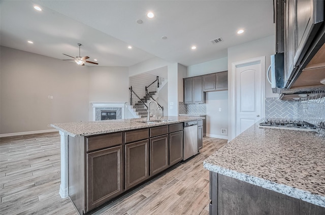 kitchen with light stone counters, light hardwood / wood-style flooring, an island with sink, and appliances with stainless steel finishes