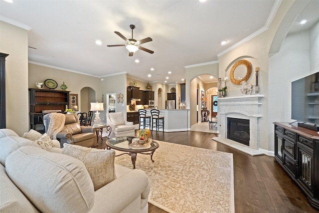 living area with dark wood-style floors, arched walkways, a glass covered fireplace, ceiling fan, and baseboards