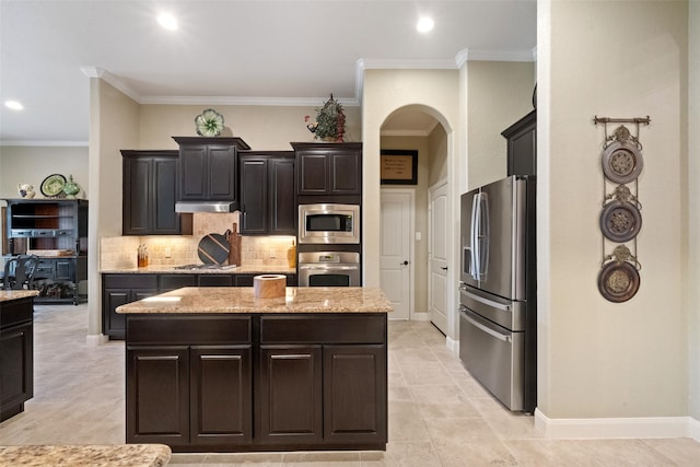 kitchen with appliances with stainless steel finishes, light stone counters, crown molding, and a center island