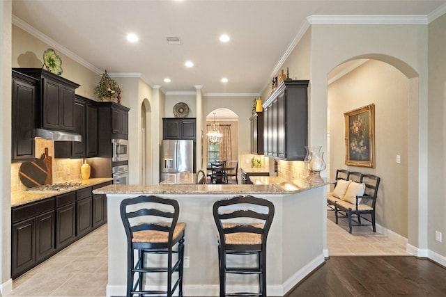 kitchen with arched walkways, a breakfast bar area, under cabinet range hood, stainless steel appliances, and visible vents