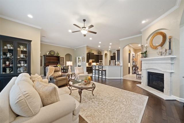 living area featuring arched walkways, dark wood-type flooring, a glass covered fireplace, ceiling fan, and baseboards