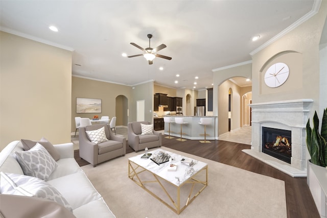 living area featuring arched walkways, recessed lighting, a lit fireplace, and wood finished floors