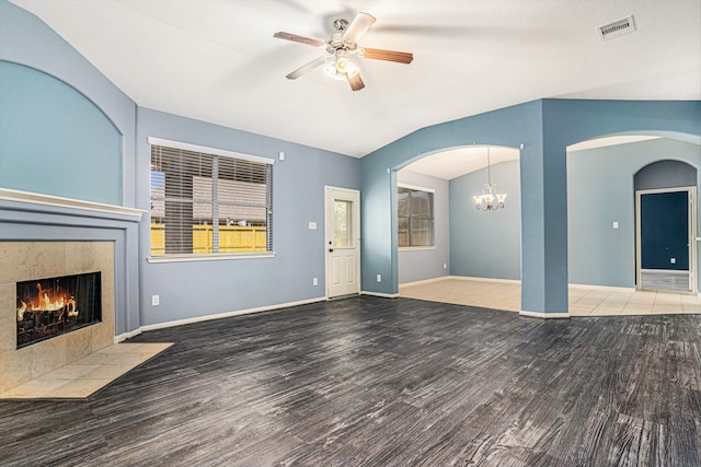 unfurnished living room with hardwood / wood-style floors, ceiling fan with notable chandelier, vaulted ceiling, and a tiled fireplace