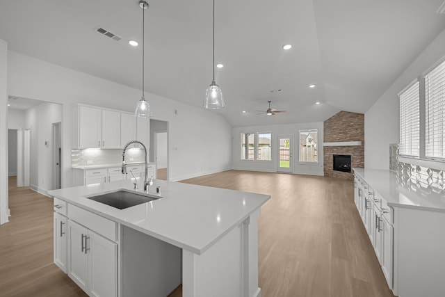 kitchen with a sink, visible vents, ceiling fan, light wood-type flooring, and a stone fireplace
