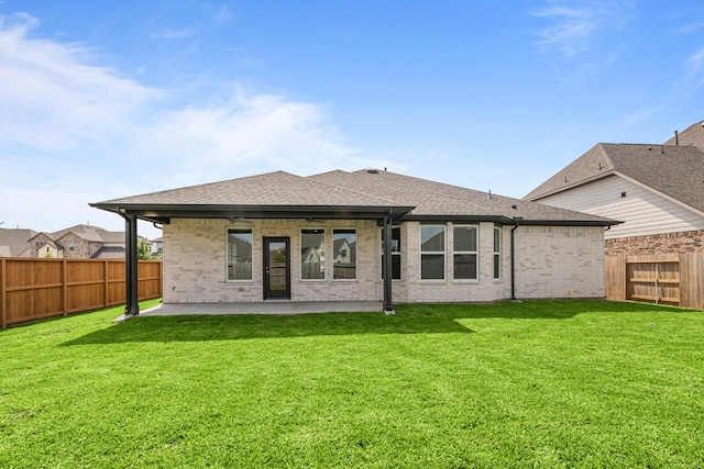 back of house with a shingled roof, a patio area, a yard, a fenced backyard, and brick siding