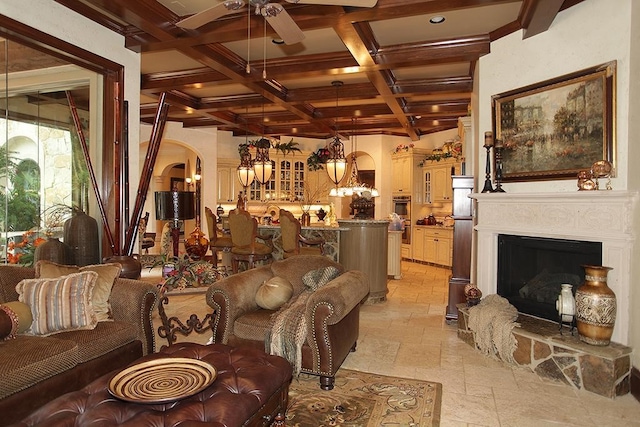 living room featuring a stone fireplace, beamed ceiling, ceiling fan, and coffered ceiling