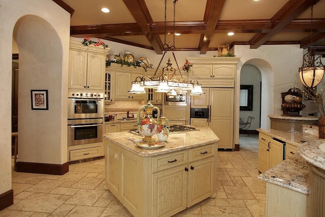 kitchen featuring light stone counters, decorative light fixtures, beamed ceiling, double oven, and a kitchen island with sink