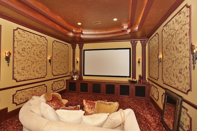 cinema featuring ornate columns, ornamental molding, a raised ceiling, and dark carpet