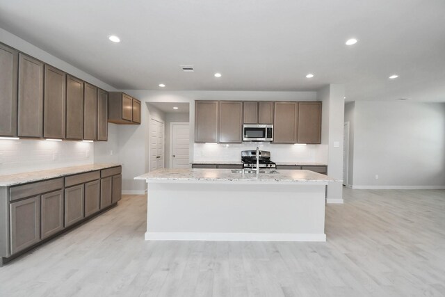 22126 Oceania Shores Dr, Hockley, TX 77447 - kitchen featuring stainless steel appliances, baseboards, tasteful backsplash, an island with sink, and light wood-style floors