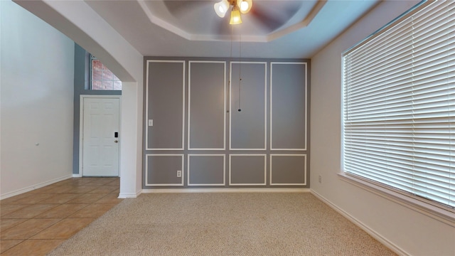 tiled spare room featuring ceiling fan and a tray ceiling